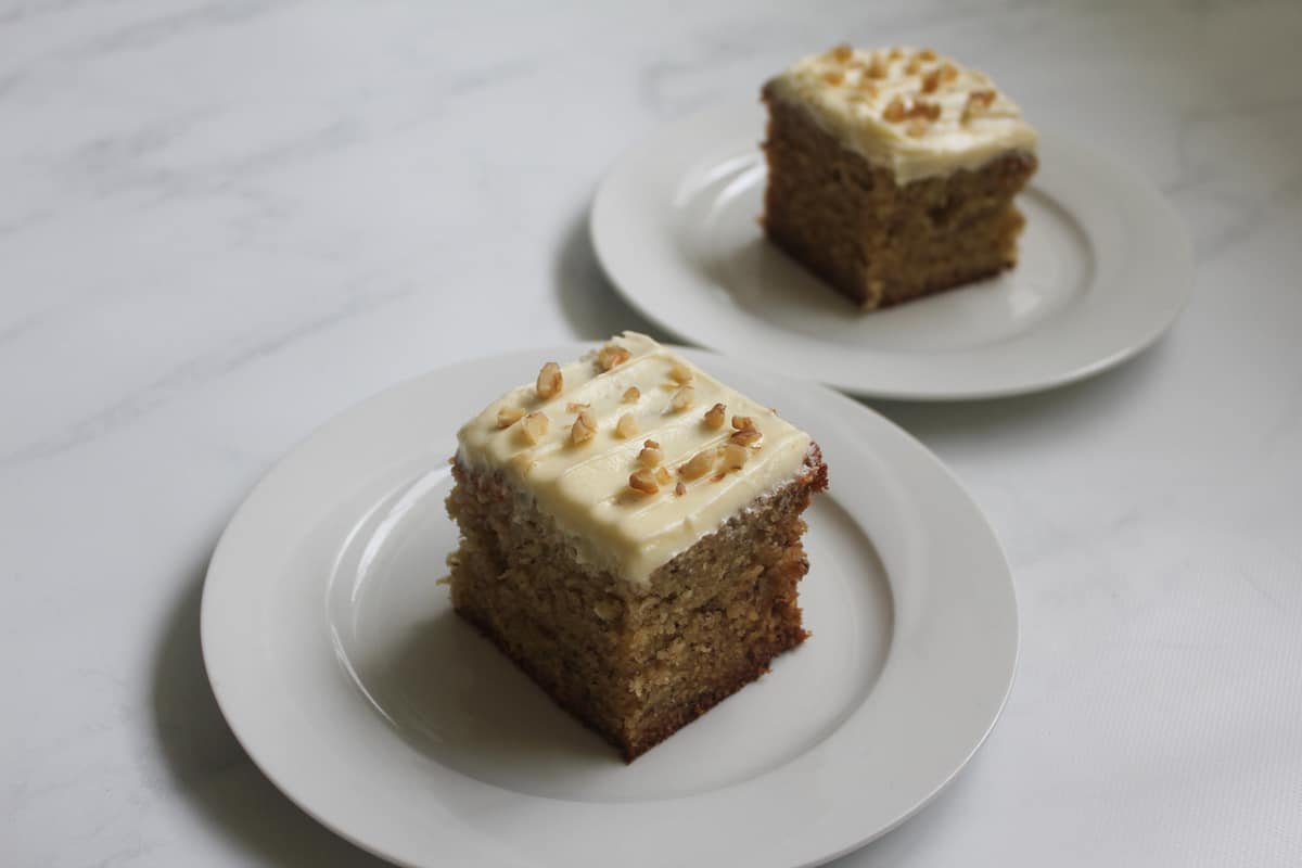 Banana cake with cream cheese icing on two plates on a white background