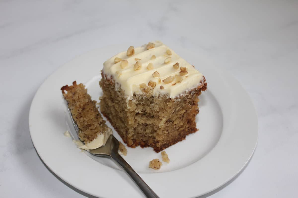 Banana Cake with Cream Cheese Icing with a fork on a white plate