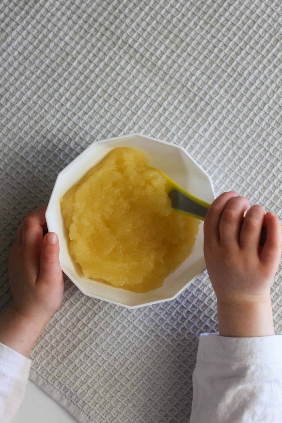 Puree in a white bowl with spoon, grey background and two hands