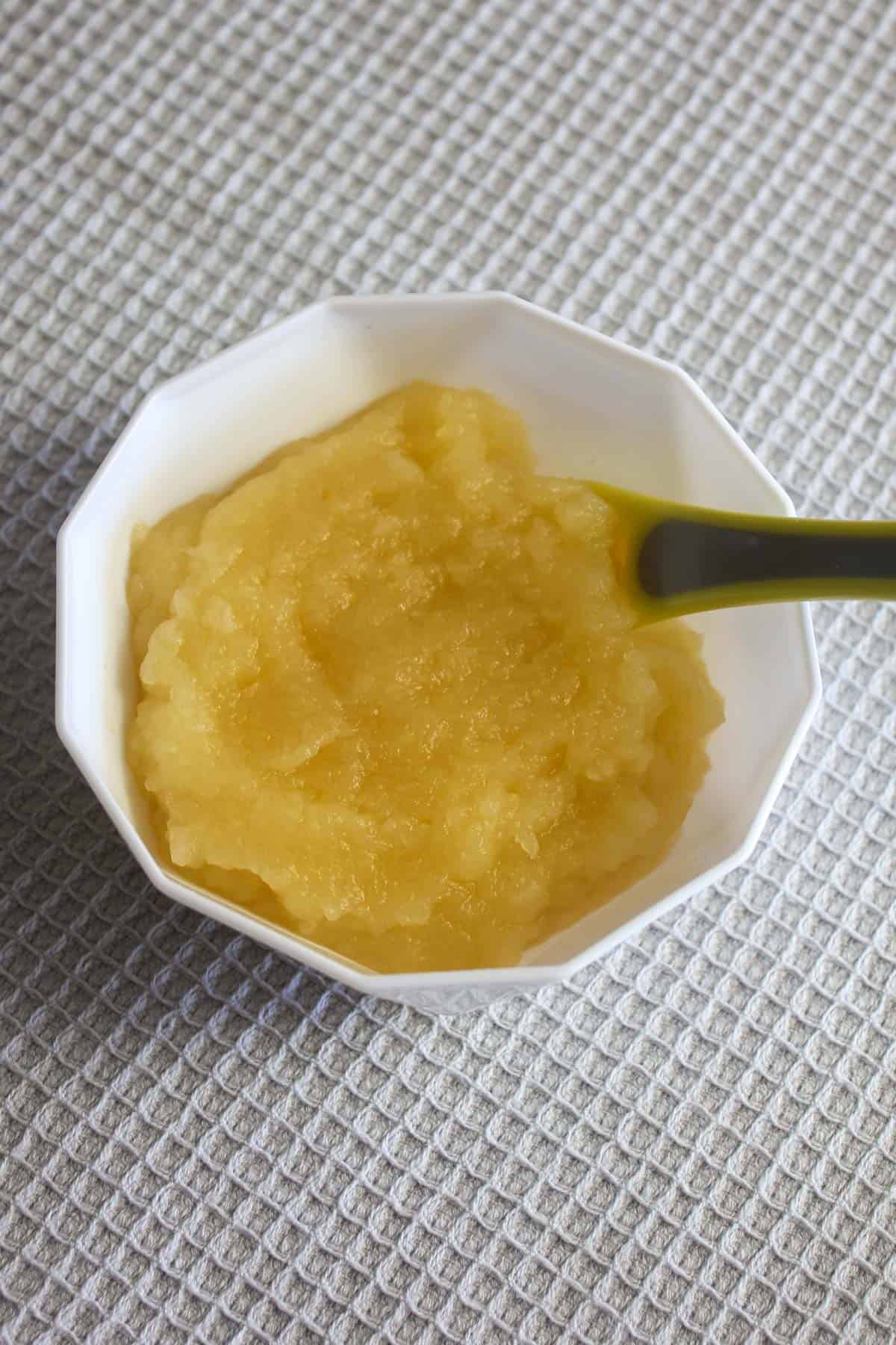 Apple puree in a white bowl with a spoon on a grey tea towel