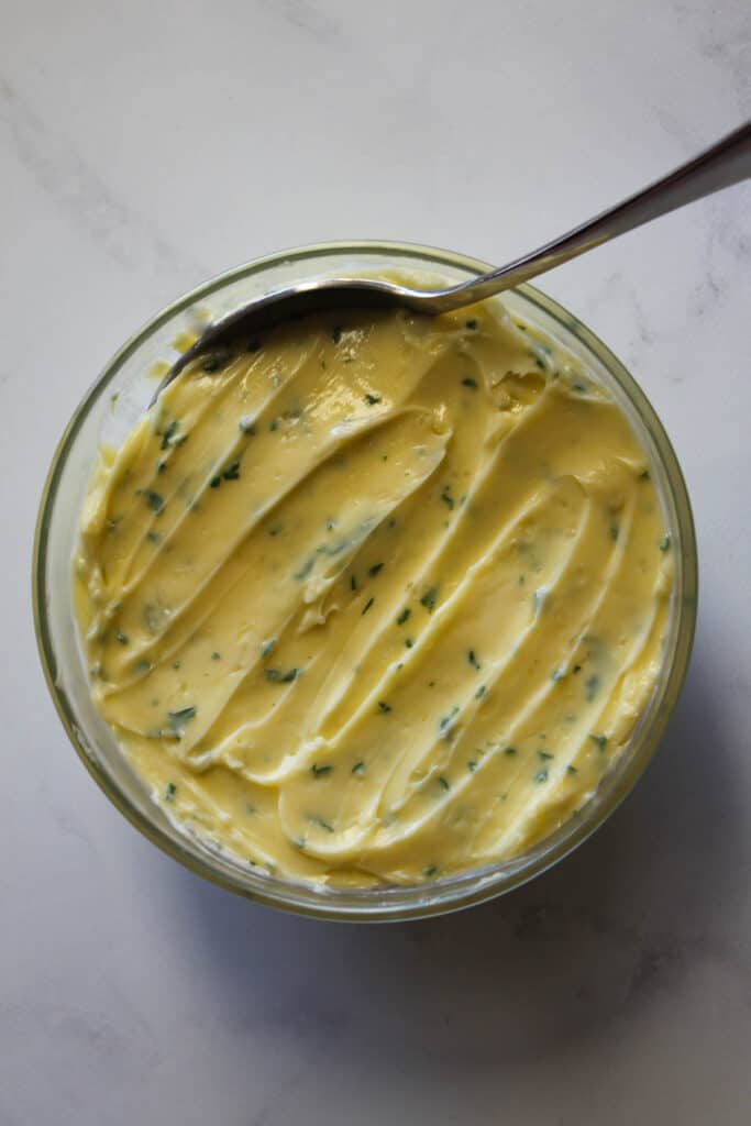 Garlic butter in a glass bowl with a spoon on a white background.