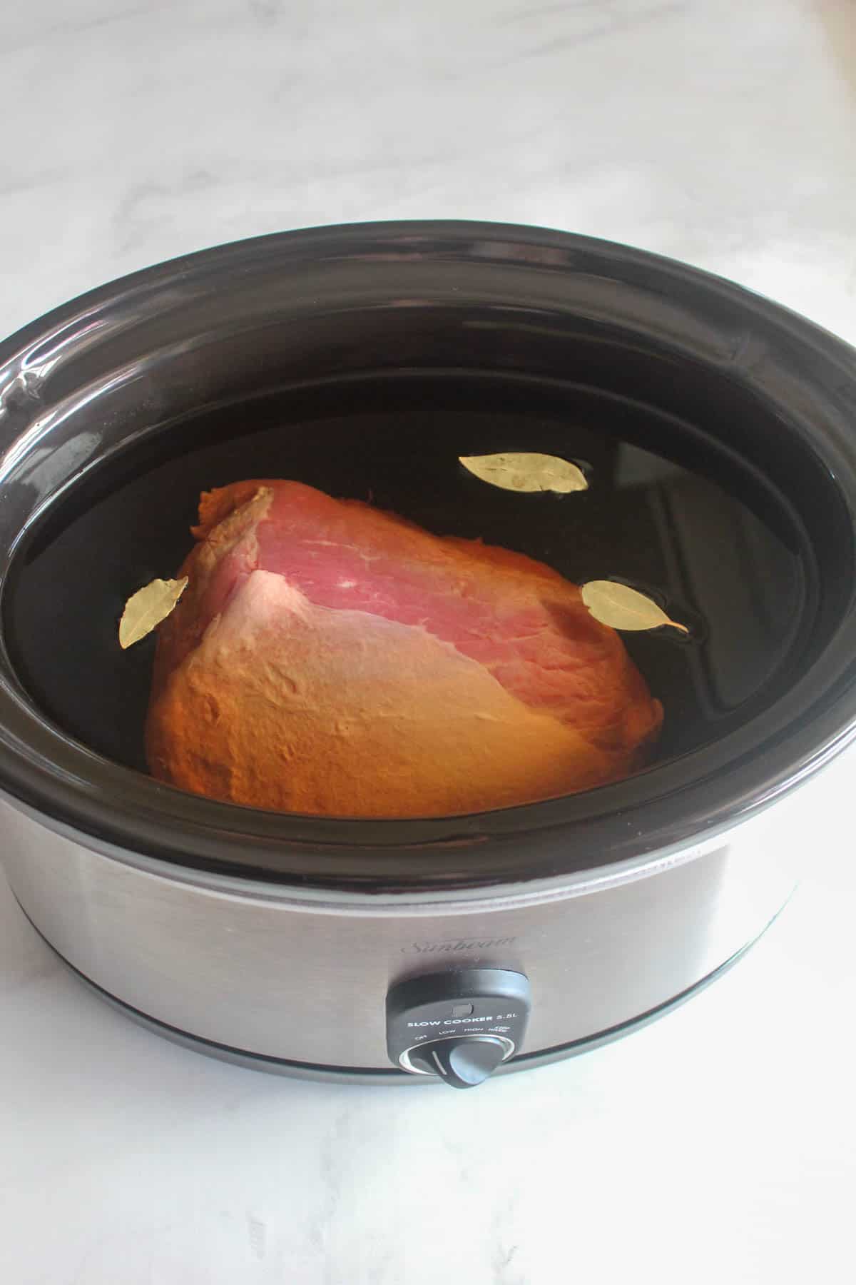Uncooked silverside placed in a slowcooker full of water and three bayleaves.