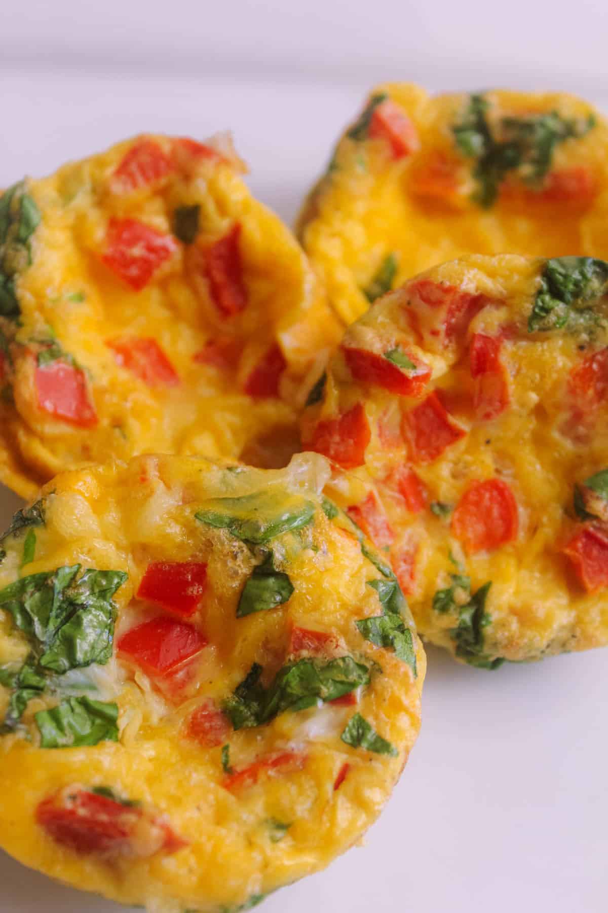 Egg, cheese, capsicum and baby spinach muffins on a white plate.