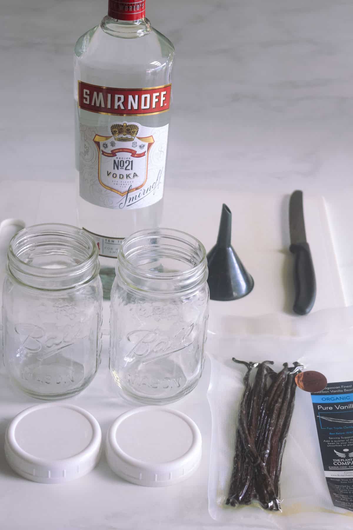Vanilla beans, knife, funnel, glass jars and vodka bottle to make homemade vanilla extract.