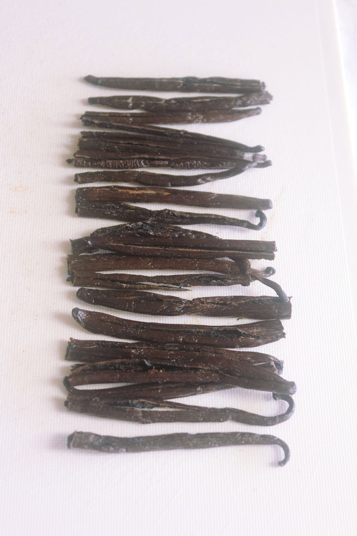 Grade B vanilla beans cut in half on a white chopping board.