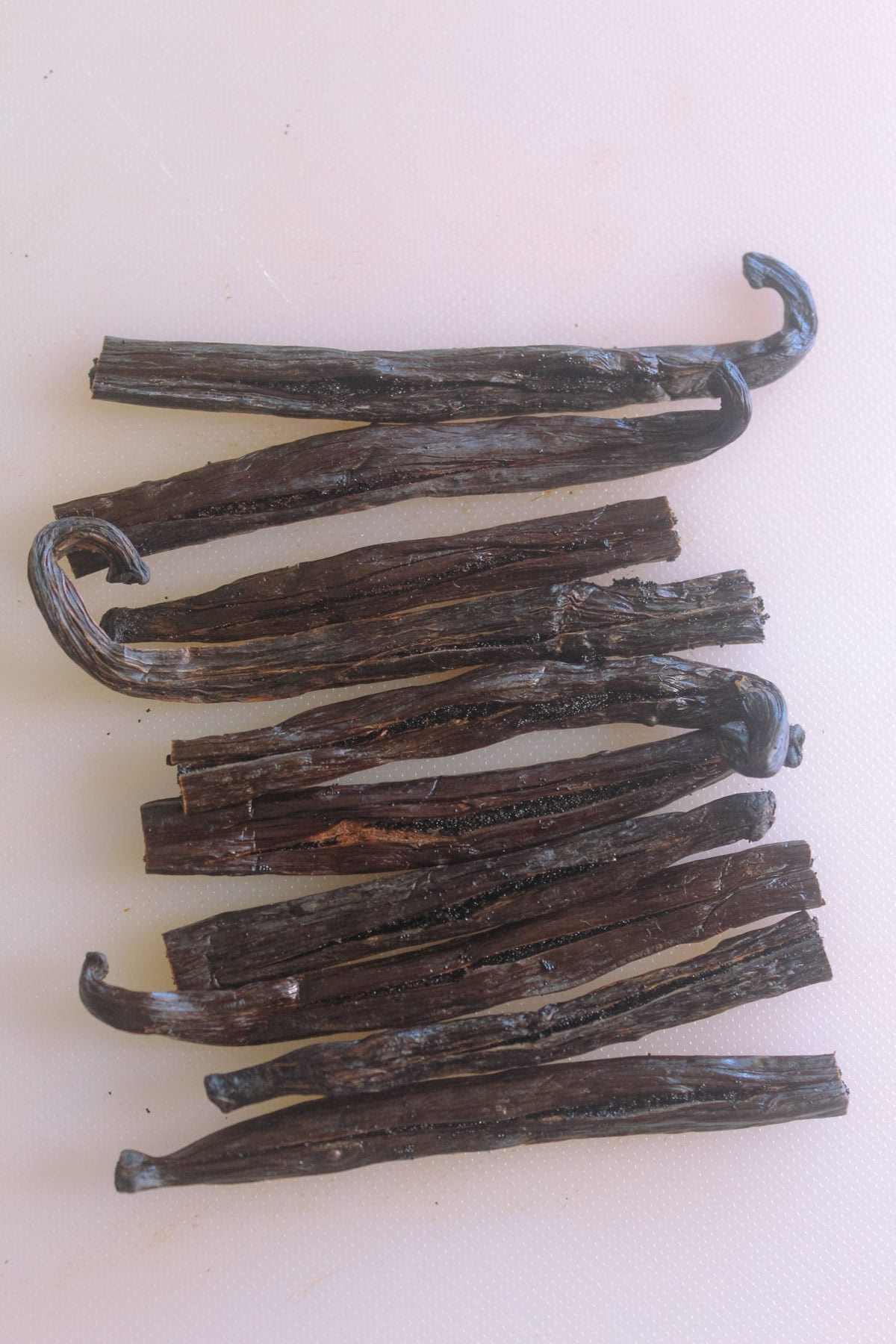 Vanilla beans are cut in half and placed on a white cutting board.