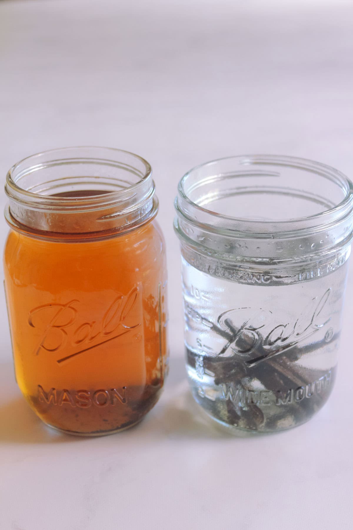 Homemade vanilla bean extract in a jar with vodka in a jar, and vanilla essence in a brown hue in another jar next to it.