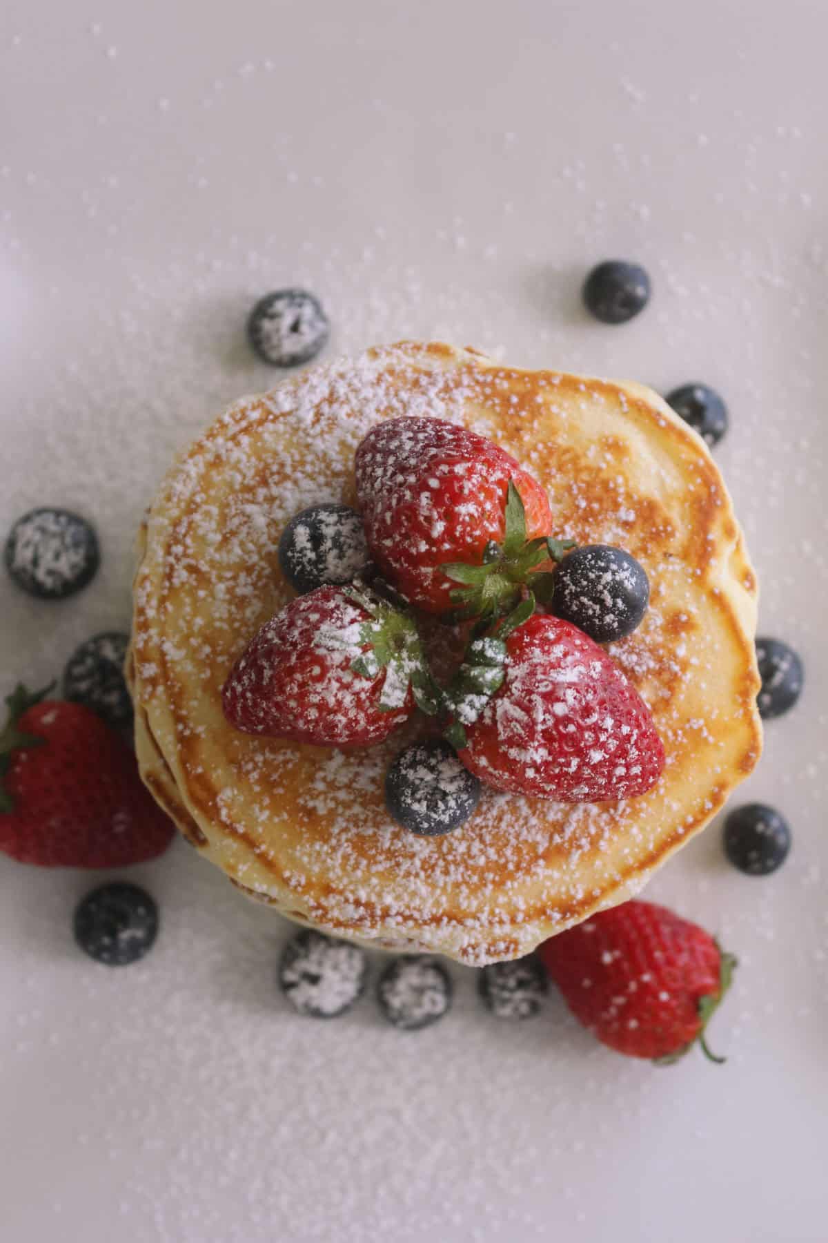 Overhead photo of pancakes with blueberries, strawberries and icing sugar over the top.