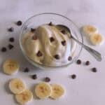 Delicious banana ice cream in a glass bowl with a spoon. Sliced bananas and choc chips displayed on a marble background