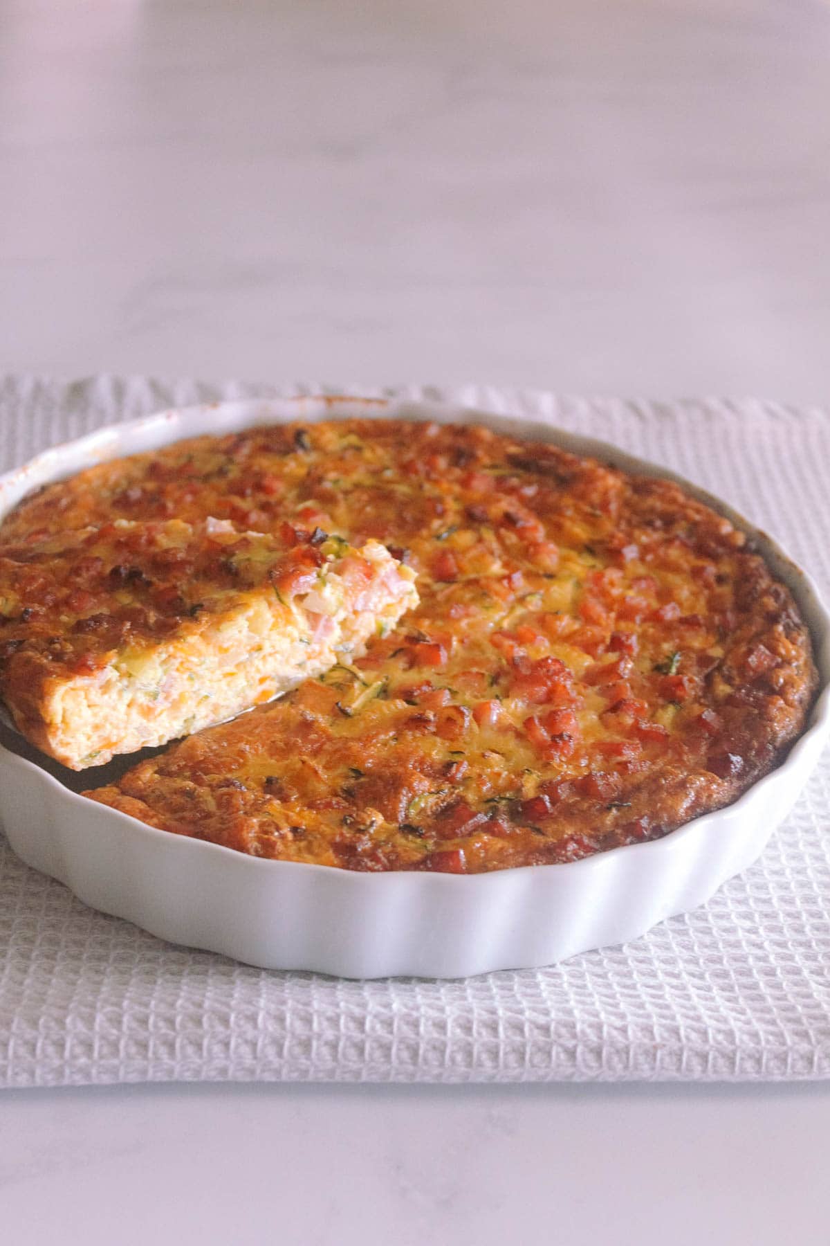 Crustless quiche in a quiche dish with a slice showing