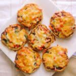 Little pizzas displayed on a white plate with a beige teatowel underneath