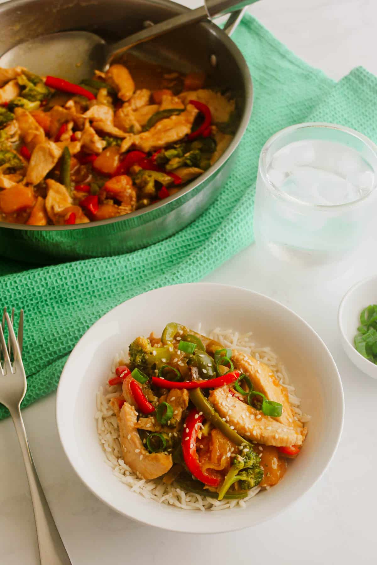 Delicious Asian stir-fry with chicken, vegetables, and rice, served with a glass of water and fresh green onions on the side. Perfect for a quick, healthy meal.
