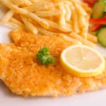 Potato chip schnitzels garnished with sliced lemon and parsley, with a side of chips and salad