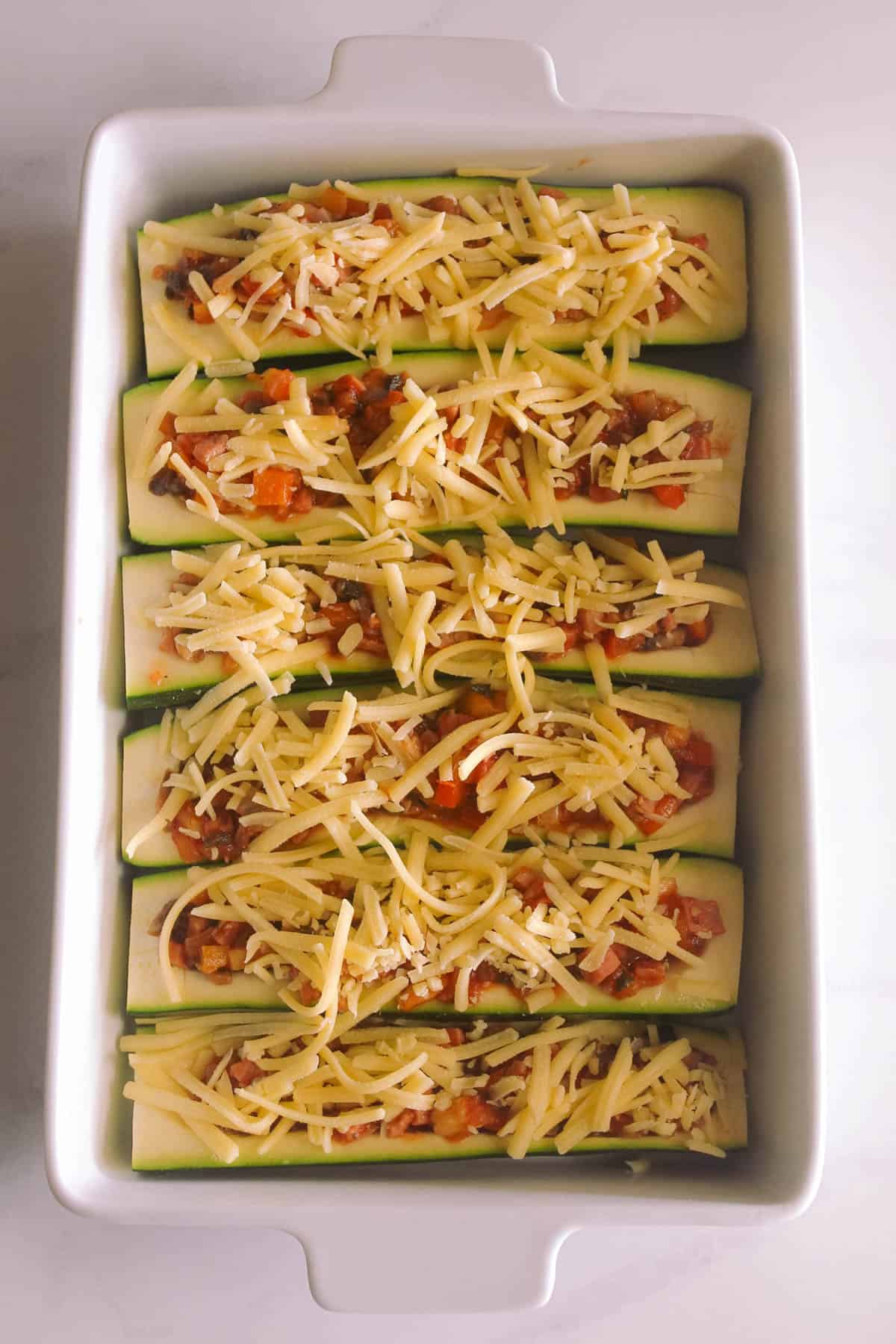 Zucchini boats filled, topped with cheese and ready to bake