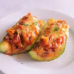 Stuffed zucchini boats on a white plate, cut in half