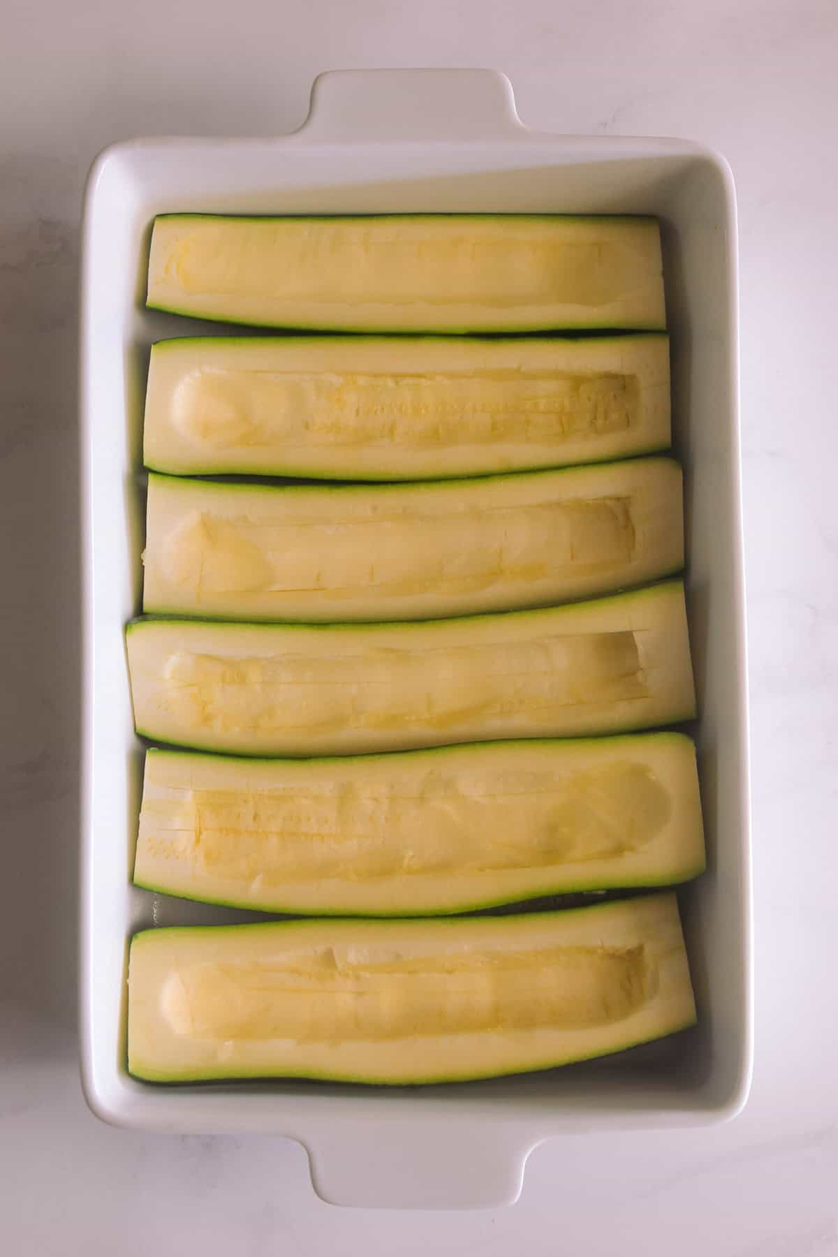 Zucchini cut in half and hollowed out, in a baking dish