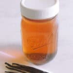 Vanilla Extract in a mason jar with a white lid and vanilla beans on a chopping board.